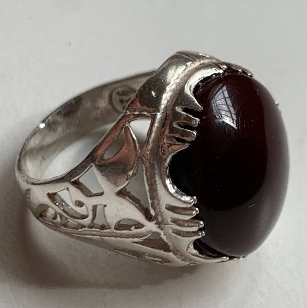 A silver ring featuring a large, polished oval dark red gemstone, photographed on a plain light background.