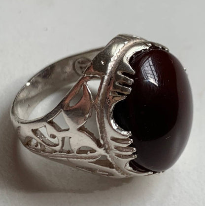 A silver ring featuring a large, polished oval dark red gemstone, photographed on a plain light background.