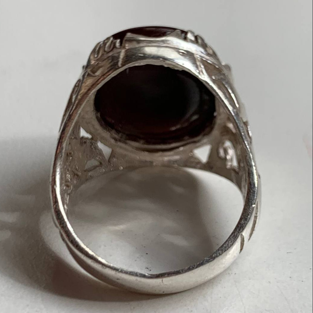 A silver filigree ring featuring a large, oval, dark reddish-brown gemstone, photographed on a plain light gray surface.